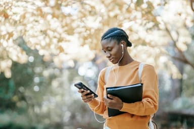 Eine Studentin nutzt ein Smartphone im Park, welches den Zugang zu Bildung und soziale Mobilität für Frauen weltweit symbolisiert