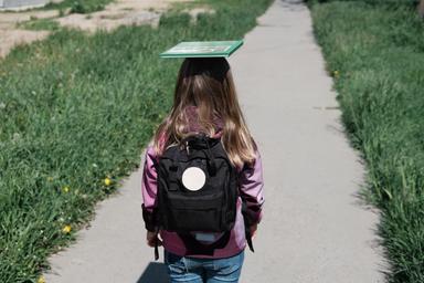 Ein Mädchen geht mit Schulrucksack auf einem Weg und symbolisiert ihren Bildungsweg.